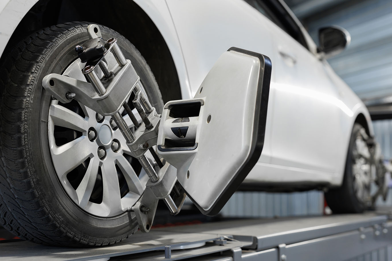 white car on a lift getting a wheel alignment. wheel alignment machines attached to front and back wheels.